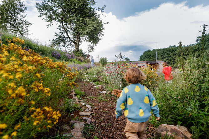 Kind läuft zu anderem Kinder im Permakulturgarten | © @titantina /Tina Vega-Wilson