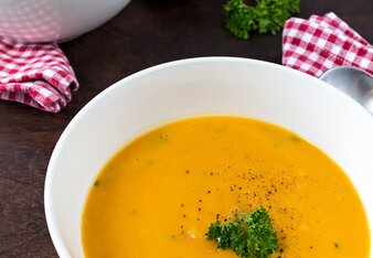 Auf dem Foto ist ein Teller mit Kürbissuppe zu sehen. Daneben sind rot-weiß karierte Stoffservietten zu sehen. | © SONNENTOR