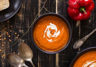 Auf dem Foto ist ein Schälchen mit Paprikaschaumsuppe zu sehen. Daneben liegen Paprika, Linsen und zwei Löffel. | © SONNENTOR