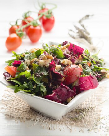 Foto vom bunten Salat. Darauf sind geröstete Walnüsse zu sehen. Im Hintergrund liegen Tomaten. | © SONNENTOR