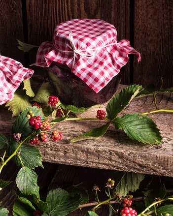 Auf dem Foto ist ein Glas mit Essig Brombeeren zu sehen. Davor sieht man einen Brombeerstrauch. | © SONNENTOR