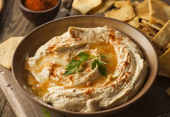 Auf dem Foto ist eine Schüssel mit Hummus zu sehen. Daneben sieht man Chips. | © SONNENTOR