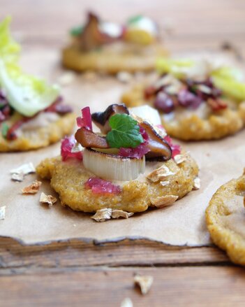 Foto von den Erdmandel Polenta Mini-Pizzen. Sie liegen auf einem Holztisch auf einem Backpapier. | © SONNENTOR