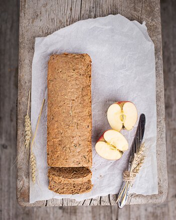 Auf dem Foto ist das Apfel-Kürbis-Brot zu sehen, daneben liegen Äpfel und Getreide. | © SONNENTOR