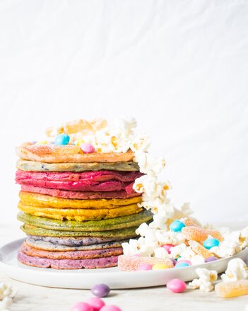 Auf dem Foto sind viel bunte Pancakes übereinander zu sehen. Von dem Turm aus Pancakes fallen Popcorn und Smarties herunter. | © SONNENTOR