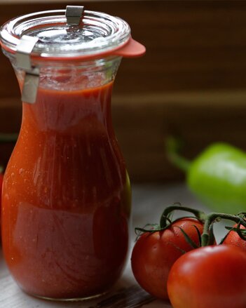 Auf dem Foto ist ein Glas gefüllt mit Gute Laune Ketchup zu sehen. Daneben liegen Tomaten. | © SONNENTOR