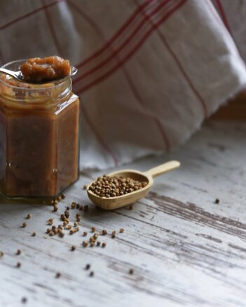 Auf dem Foto sieht man ein Glas mit Rhabarber-Koriander-Chutney. Daneben sieht man Koriander Körner. | © SONNENTOR