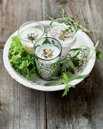 Auf dem Foto sind drei Gläser mit Schutzengel Dressing zu sehen. Daneben liegen frische Kräuter und Blattsalat. | © SONNENTOR