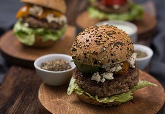 Auf dem Foto sind Burger Greek Style auf Holztellern zu sehen. Darauf steht auch eine kleine Schüssel mit Gewürzen. | © SONNENTOR