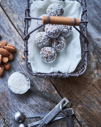 Auf dem Foto sind in einem Körbchen mehrere Espresso Energy Balls zu sehen. Daneben sind Mandeln und Kokosraspeln zu sehen. | © SONNENTOR