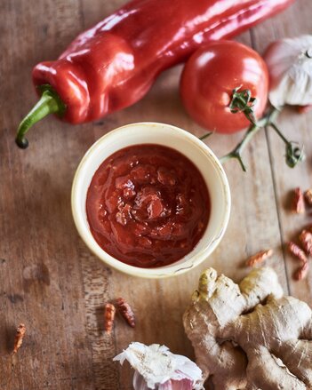 Auf dem Foto sieht man ein Schälchen mit süßer Chili Sauce. Daneben sind Ingwer, Knoblauch, Paprika,  Tomaten und Chili zu sehen. | © SONNENTOR