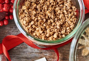 Auf dem Foto sieht man ein Glas mit Lebkuchen-Granola. Davor sieht man ein Etikett, das auf einem roten Band befestigt ist. | © SONNENTOR