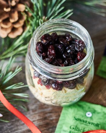 Auf dem Foto ist ein Glas mit Porridgemischung zu sehen. Daneben liegen eine Sonnentorteepackung, Zapfen und Tannenzweige. | © SONNENTOR