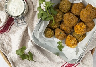 Auf dem Foto ist eine Box mit Hülsenfrüchtebällchen zu sehen. Daneben sieht man ein Glas mit Dip. | © SONNENTOR