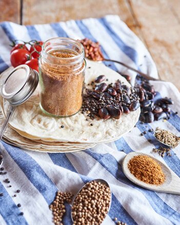 Auf dem Foto sieht man mehrere Tortilla-Scheiben. Darauf steht ein Glas mit Taco-Gewürzmischung. Daneben sind verschiedenes Gemüse und Kräuter zu sehen. | © SONNENTOR