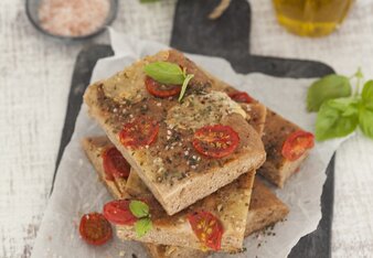 Auf dem Foto sieht man mehrere Vollkorn-Focaccia mit Tomate und Mozzarella. Im Hintergrund sieht man das ätherische Öl des Basilikums. | © SONNENTOR