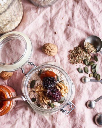 Auf dem Foto ist ein Glas Power-Porridge zu sehen. Daneben liegen Walnüsse, Kürbiskerne und Gewürze. | © SONNENTOR