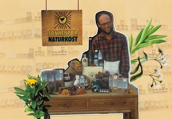 Auf dem Foto steht Hannes 1991 hinter einem Verkaufsstand mit einigen Produkten und darüber mit dem Schild "SONNENTOR Naturkost" darüber.  | © SONNENTOR