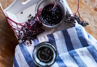 Auf dem Foto sieht man ein Glas mit Hollerkoch. Daneben sieht man frische Hollunderbeeren. | © SONNENTOR