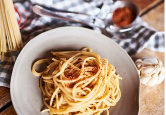 Auf dem Foto ist ein Teller mit Spaghetti aglio e olio zu sehen. Neben dem Teller sieht man Knoblauch, Tomaten und ungekochte Nudeln. | © SONNENTOR