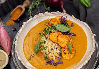 Auf dem Foto ist eine Schale Süßkartoffel-Kurkuma Suppe zu sehen. Darin sind Nudeln, Süßkartoffelchips und Spinatblätter zu sehen. | © SONNENTOR