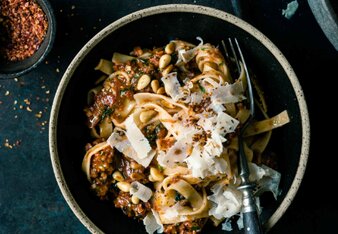 Auf dem Foto ist ein schwarzer Teller mit Tomatenpesto Pasta zu sehen. Darüber sind Nüsse, Parmesan und Chiliflocken gestreut. | © SONNENTOR