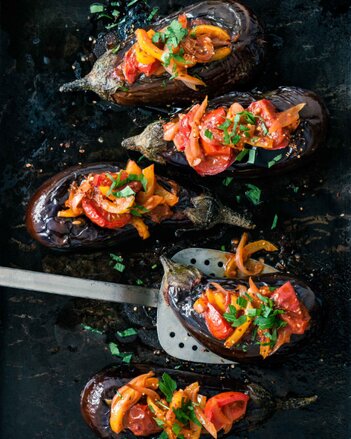 Foto von mehreren gefüllten Auberginen. Auf den Auberginen sind Tomaten, Paprika und Petersilie zu sehen. | © SONNENTOR