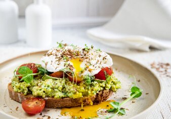 Auf dem Foto ist ein Brot zu sehen, das mit Erbsen-Mash, Tomaten und Spiegelei belegt ist. Als Topping sind diverse Kräuter zu sehen. | © SONNENTOR