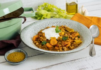 Auf dem Foto sieht man einen Teller mit Linsen-Curry-Eintopf. Der Eintopf ist mit einen Klacks Sauerrahm und Petersilie angerichtet. | © SONNENTOR