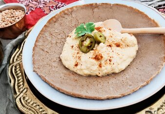 Auf dem Foto sieht man Injera mit Shiro darauf. Im Hintergrund ist eine Schüssel mit Kichererbsen zu sehen. | © SONNENTOR