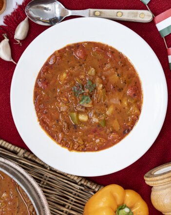 Auf dem Foto sieht man einen Teller mit ungarischer, veganer Gulaschsuppe. Daneben sieht man Paprika und Knoblach. | © SONNENTOR