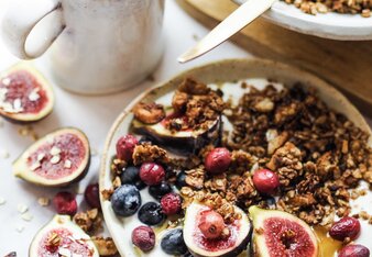 Auf dem Foto ist ein Teller mit Granola und frischen Früchten zu sehen. Daneben steht eine Tasse Rooibos Orangen Tee. | © SONNENTOR