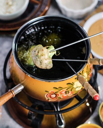 Auf dem Foto sieht man einen Topf mit Öl darin. Auf den Fondue Spießen ist Gemüse mit Teig zu sehen. das Gemüse wird im Öl gebacken. | © SONNENTOR