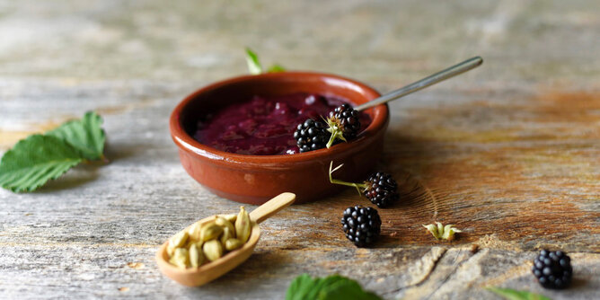 Auf dem Foto sieht man eine Schale Brombeermarmelade. Daneben sieht man auch noch frische Brombeeren und Kardamomkapseln. | © SONNENTOR