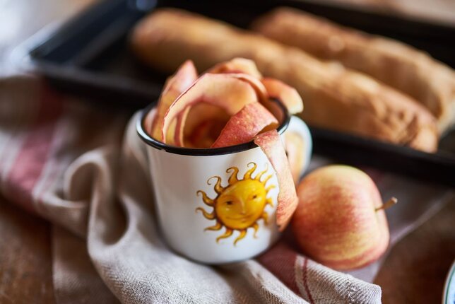 Auf dem Foto sieht man eine Sonnentor Tasse mit Apfelschale. Im Hintergrund sieht man auf einem Blech zwei Strudel. | © SONNENTOR