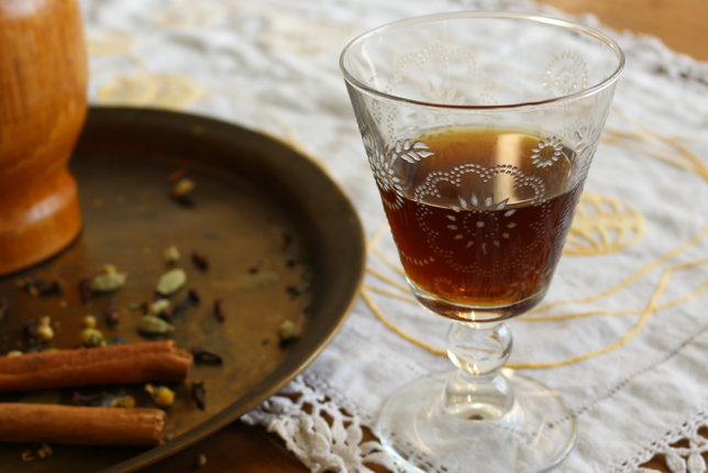 Auf dem Foto sieht man ein Glas mit Kräuterbitter. Daneben sieht man Kardamom, Nelken und Zimt. | © SONNENTOR