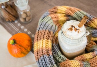 Auf dem Foto ist ein Glas mit Pumpkin Spice Latte zu sehen. Das Glas ist mit einem Schal umhüllt. Daneben liegt ein kleiner Kürbis. | © SONNENTOR