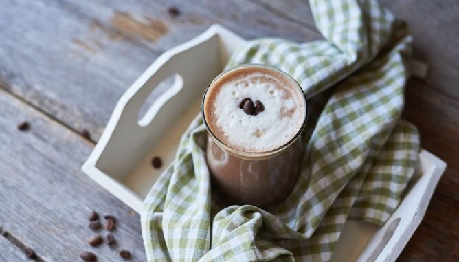 Auf dem Foto sieht man ein Glas Kaffee Smoothie. Es steht auf einem weißen Tablett mit einem grün-weißem Tuch darauf. | © SONNENTOR