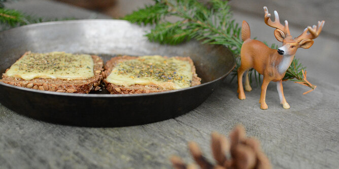 Auf dem Foto sind zwei Raclette Brote zu sehen. Daneben sieht man Zweige, Zapfen und einen Schleich Hirsch. | © SONNENTOR