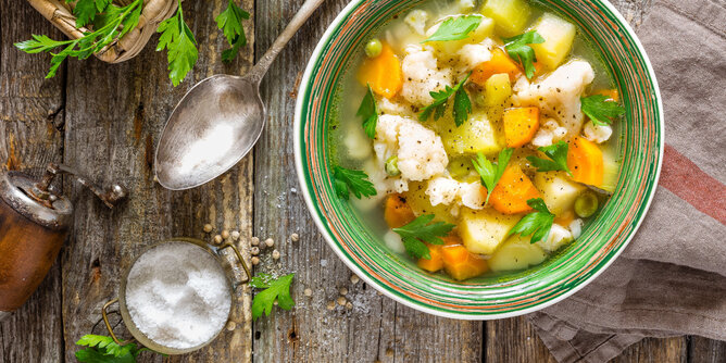 Auf dem Foto sieht man eine Schüssel mit Basenfasten Suppe. Daneben sind Gewürze und frische Petersilie zu sehen. | © SONNENTOR