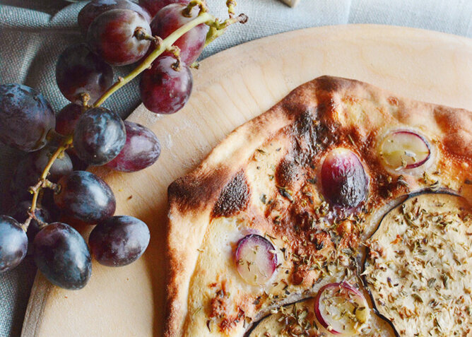 Auf dem Foto sieht man Focaccia mit roten Trauben darauf. Darüber sind verschiedene Kräuter gestreut. | © SONNENTOR